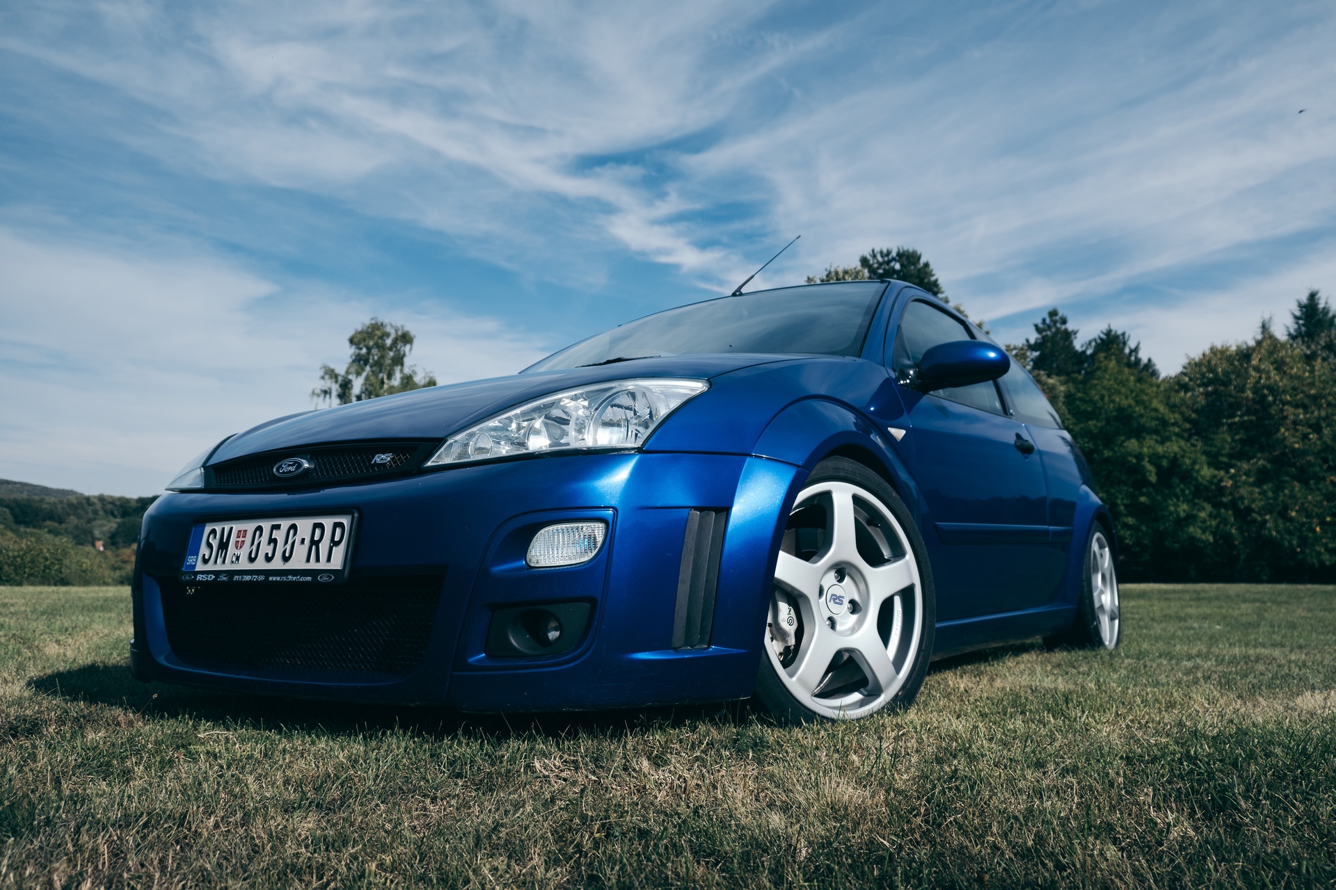 Front and left side view of blue Ford Focus RS in field near forest