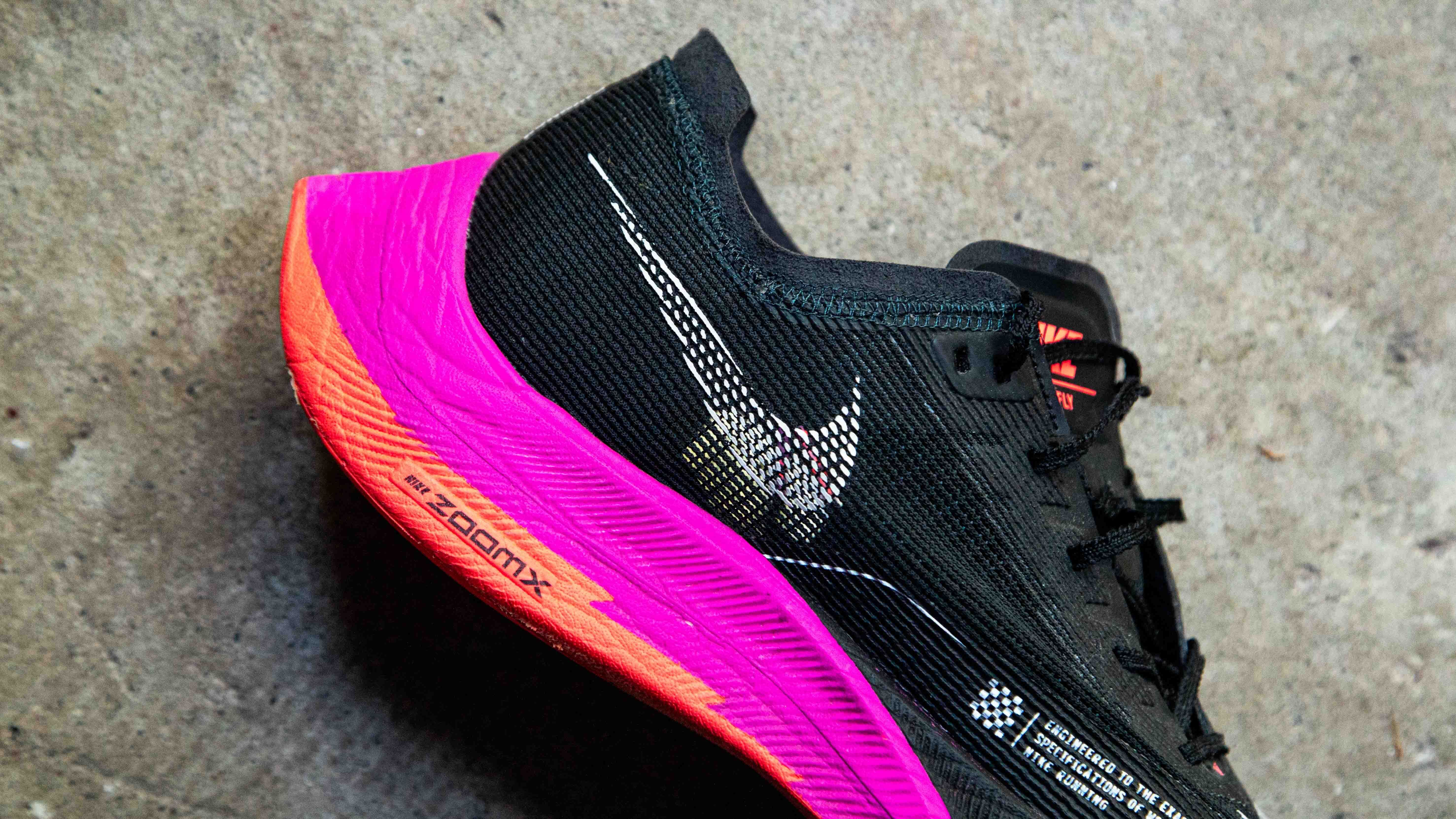 black nike running shoe with a pink sole laying on a concrete surface