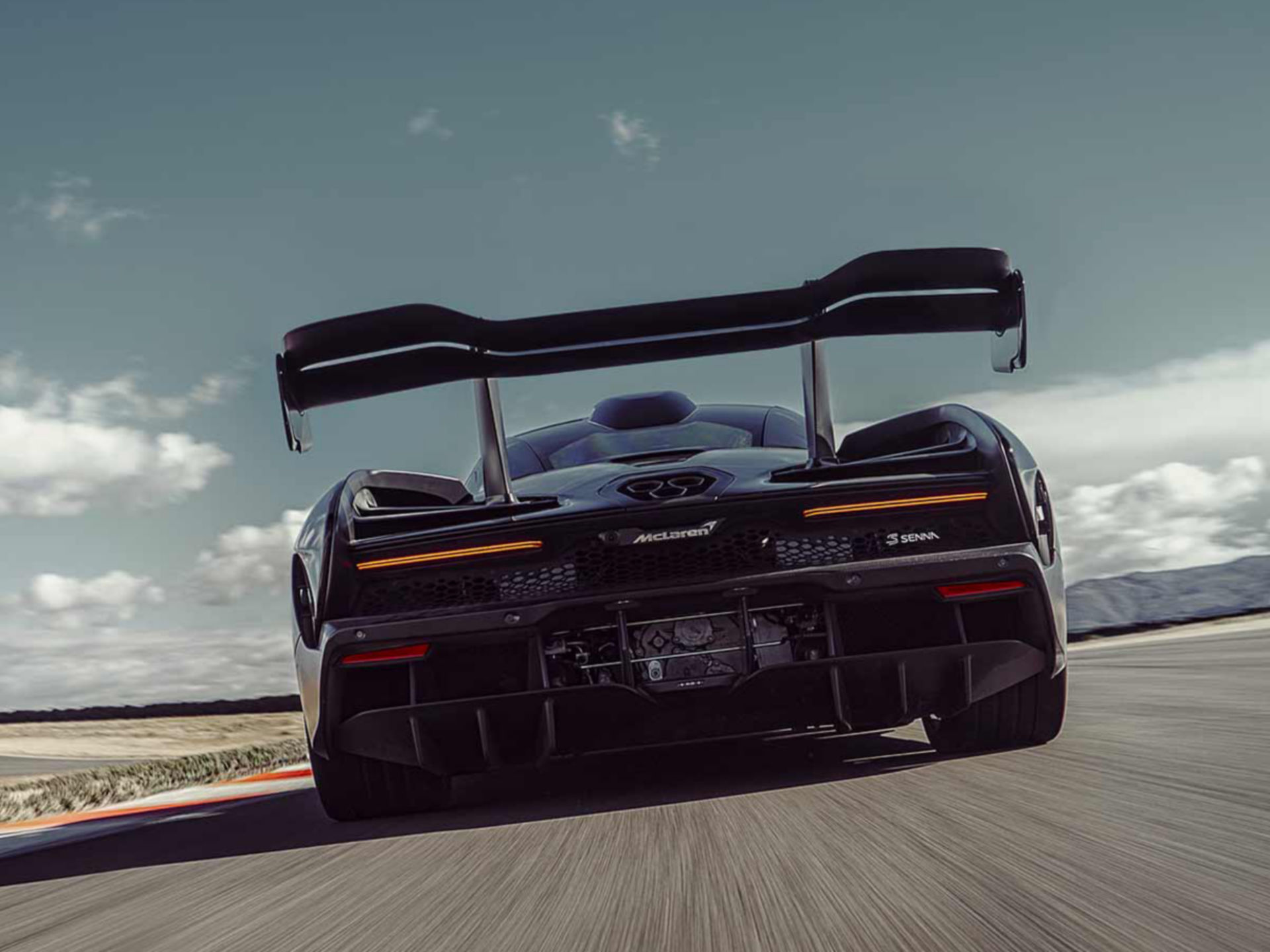 Rear view of black McLaren Senna being driven down track at high speed