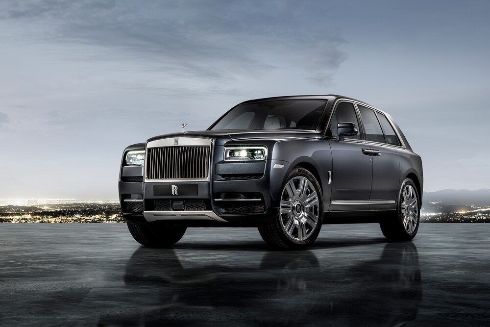 Black Rolls Royce Cullinan parked on tarmac with city lights in background